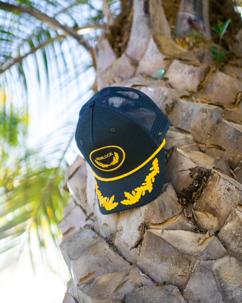 Hemlock Captain Trucker Hat in Navy by palm tree