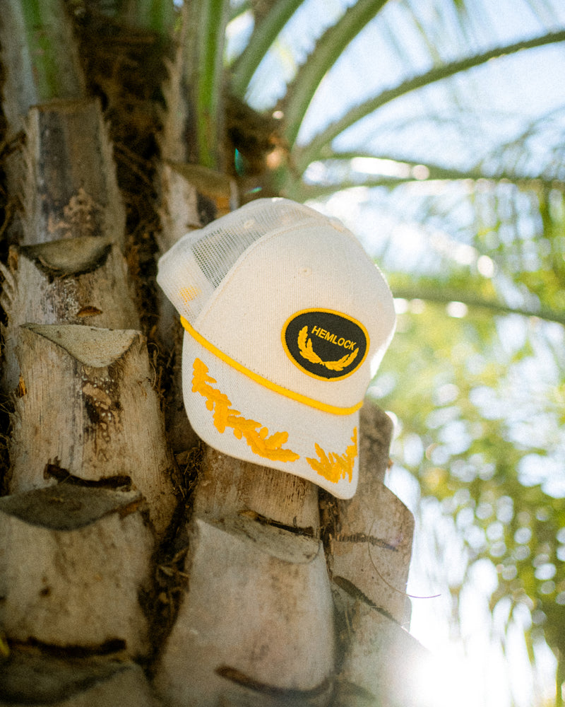 Hemlock Captain Trucker Hat by a palm tree