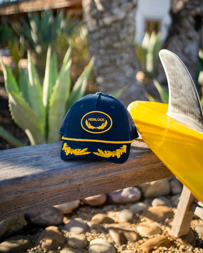 Hemlock Captain Trucker Hat in Navy by surfboard