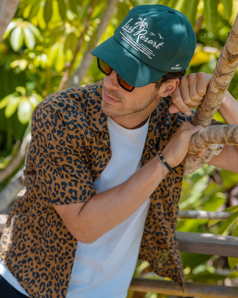 Hemlock male model wearing the Last Resort Baseball Hat in Green with cheetah print shirt