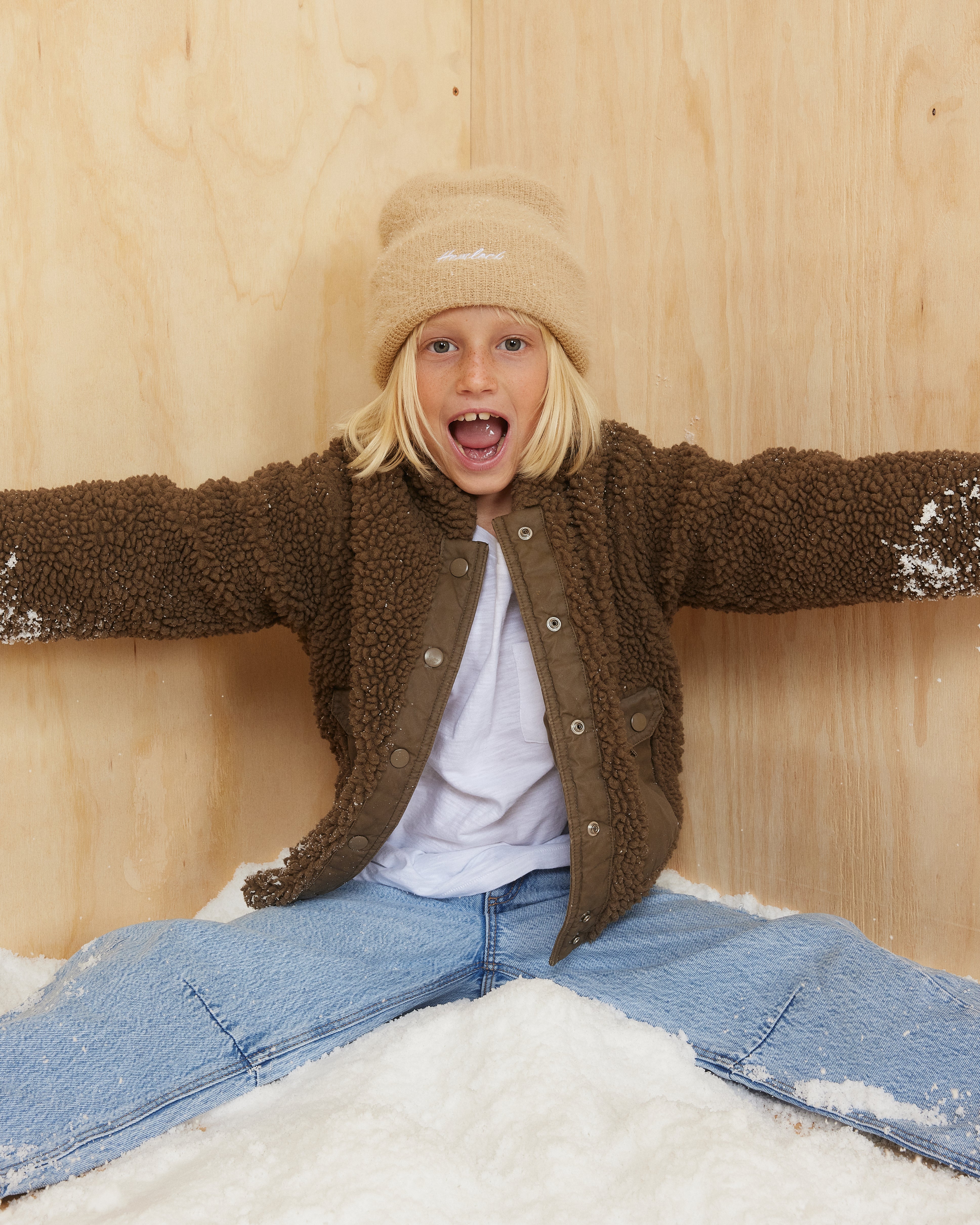 Hemlock little girl wearing the Toddler Ivy Fuzzy Beanie in Oat color sitting on snow