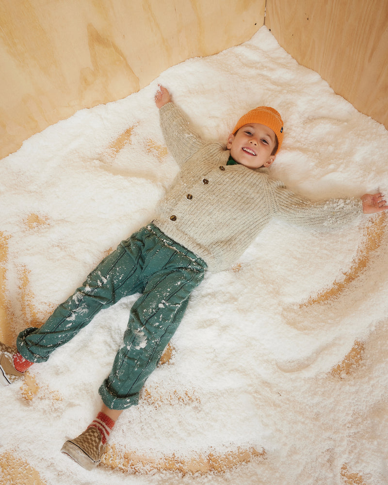 Hemlock little boy model wearing the Toddler Ranger Beanie in Apricot color playing with snow