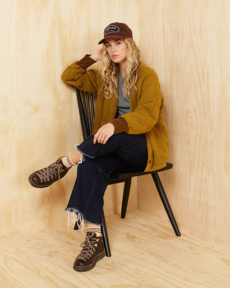 Hemlock female model wearing the Palomar Baseball Hat in Tobacco color with legs crossed